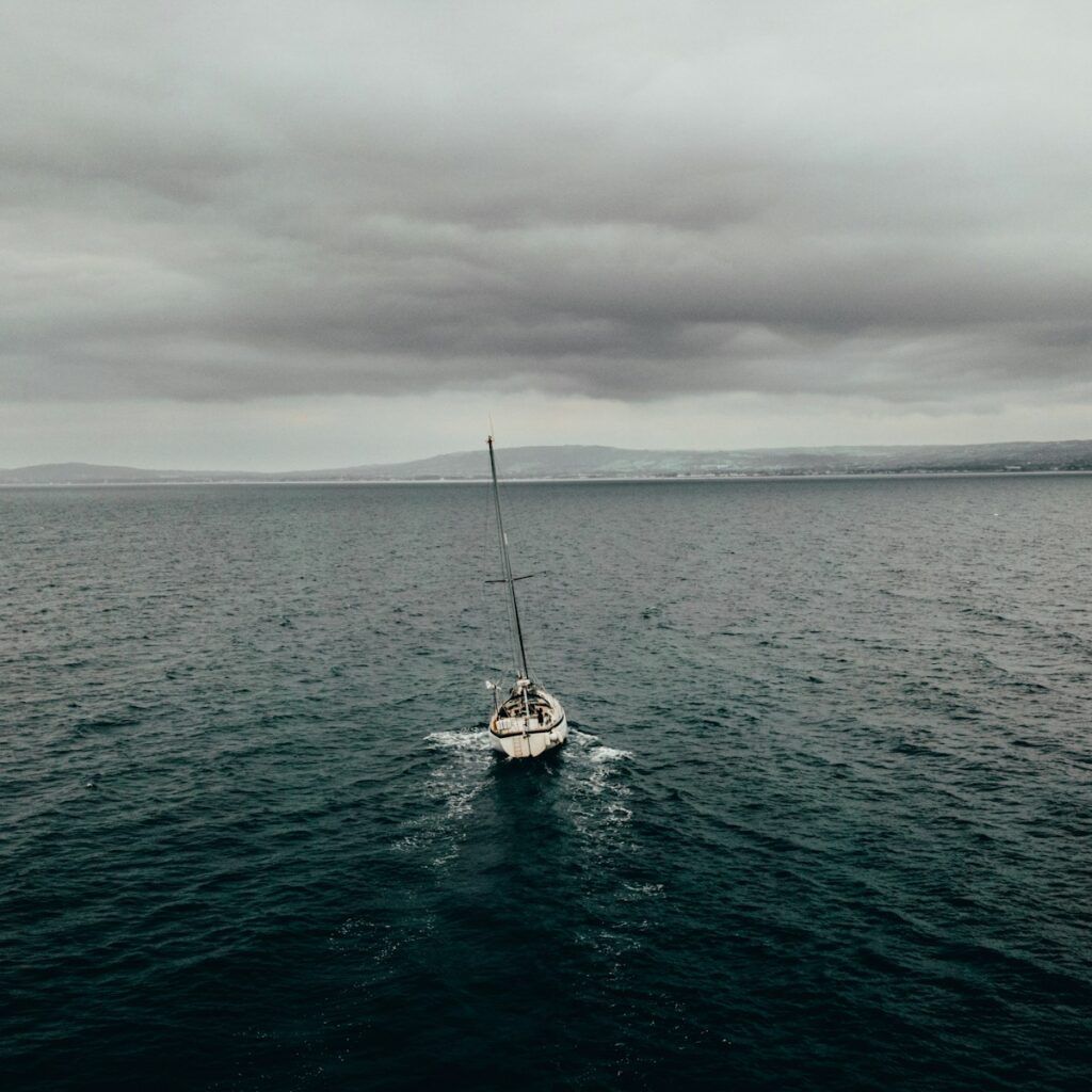 white sailboat on sea under gray sky